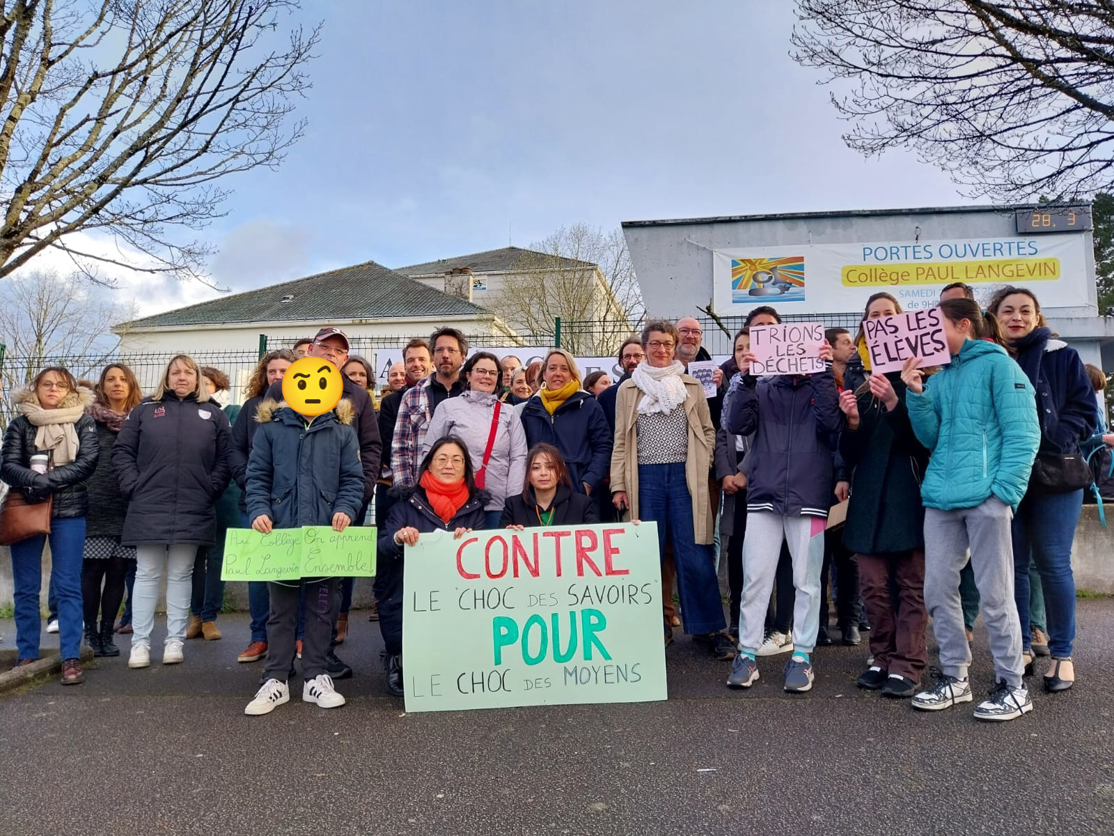 Photo d'un groupe de parents ainsi que quelques enfants visages masqués devant le collège Paul Langevin. Ils portent des écriteaux, «Au collège … on apprend ensemble», «Contre le choc des savoirs pour le choc des moyens», «Trions les déchets», «pas les élèves»